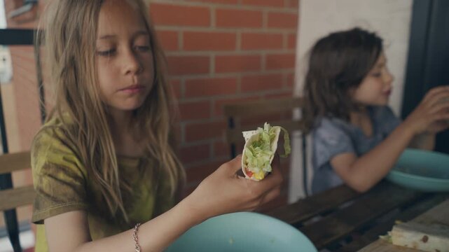 Children eating vegetable wraps at a wooden patio table