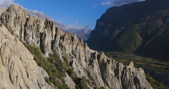 Annapurna Circuit, Manang, Nepal, aerial sideways gliding shot of unique jagged rock formations and cliffs overlooking a deep mountain valley on a clear blue day