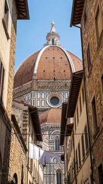 Iconic view of the Cathedral of Santa Maria del Fiore in Florence, Italy, framed by narrow historic stone buildings under a clear blue sky, showcasing Brunelleschi's magnificent Renaissance dome.