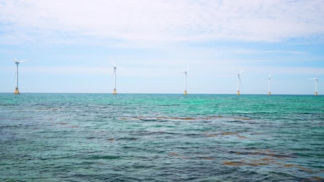 Row of offshore wind turbines spans the horizon above calm turquoise water at Singgyemul Park on Jeju Island