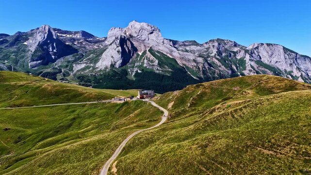 Winding road curves toward Table de l Aubisque rest stop beneath jagged limestone peaks of Cirque de Gourette in Pyrenees