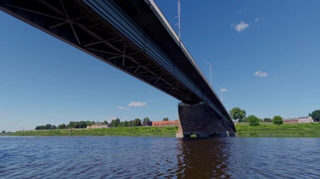 Looking up at steel truss structure and concrete deck of Vienibas Unity bridge spanning calm Daugava river on sunny day in Daugavpils city, Latvia.