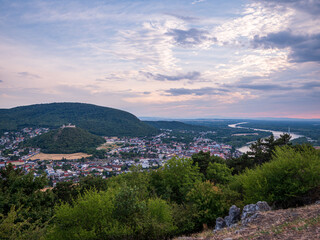 Fototapeta premium Panoramic view from Braunsberg Hill overlooking Hainburg an der Donau, the Danube River and Schlossberg Castle at sunset under dramatic evening clouds in Austria.