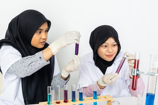 Two Muslim female scientists wearing hijab working in a chemistry laboratory with glassware and chemical solutions. Perfect for STEM education, research, science, healthcare, and biotechnology concept