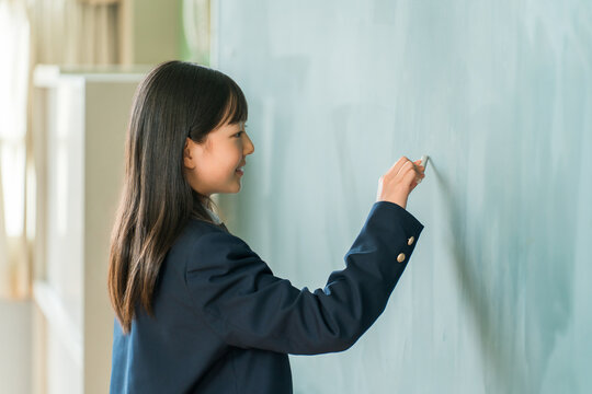 A middle school girl writing on the classroom blackboard with chalk.