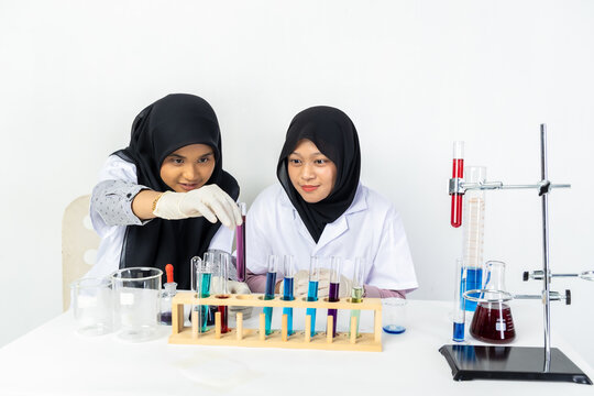 Two Muslim female scientists wearing hijab working in a chemistry laboratory with glassware and chemical solutions. Perfect for STEM education, research, science, healthcare, and biotechnology concept