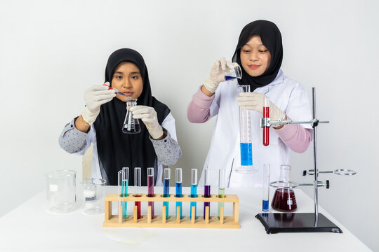 Two Muslim female scientists wearing hijab working in a chemistry laboratory with glassware and chemical solutions. Perfect for STEM education, research, science, healthcare, and biotechnology concept