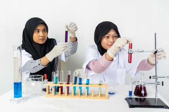 Two Muslim female scientists wearing hijab working in a chemistry laboratory with glassware and chemical solutions. Perfect for STEM education, research, science, healthcare, and biotechnology concept