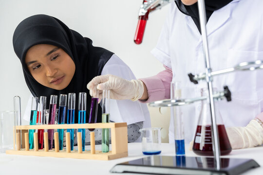 Two Muslim female scientists wearing hijab working in a chemistry laboratory with glassware and chemical solutions. Perfect for STEM education, research, science, healthcare, and biotechnology concept