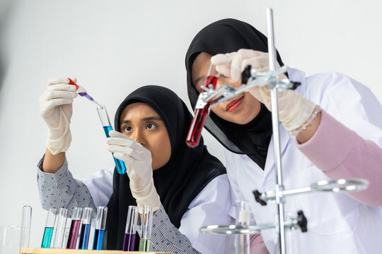 Two Muslim female scientists wearing hijab working in a chemistry laboratory with glassware and chemical solutions. Perfect for STEM education, research, science, healthcare, and biotechnology concept