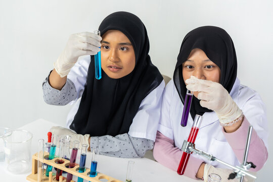 Two Muslim female scientists wearing hijab working in a chemistry laboratory with glassware and chemical solutions. Perfect for STEM education, research, science, healthcare, and biotechnology concept
