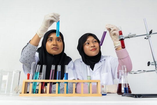 Two Muslim female scientists wearing hijab working in a chemistry laboratory with glassware and chemical solutions. Perfect for STEM education, research, science, healthcare, and biotechnology concept