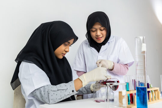 Two Muslim female scientists wearing hijab working in a chemistry laboratory with glassware and chemical solutions. Perfect for STEM education, research, science, healthcare, and biotechnology concept