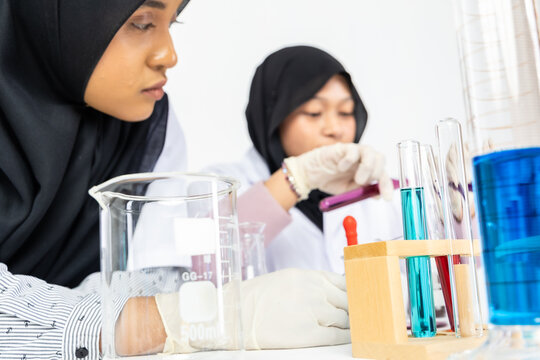 Two Muslim female scientists wearing hijab working in a chemistry laboratory with glassware and chemical solutions. Perfect for STEM education, research, science, healthcare, and biotechnology concept