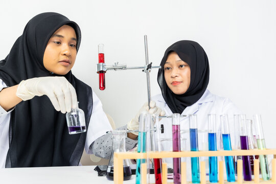Two Muslim female scientists wearing hijab working in a chemistry laboratory with glassware and chemical solutions. Perfect for STEM education, research, science, healthcare, and biotechnology concept