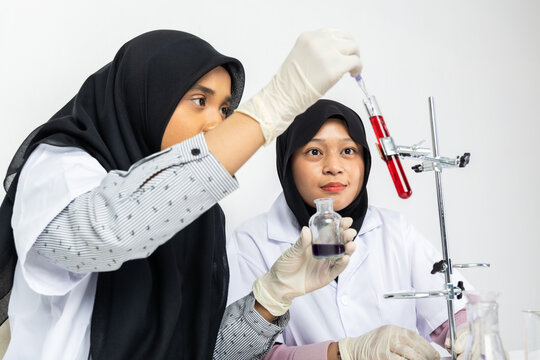 Two Muslim female scientists wearing hijab working in a chemistry laboratory with glassware and chemical solutions. Perfect for STEM education, research, science, healthcare, and biotechnology concept