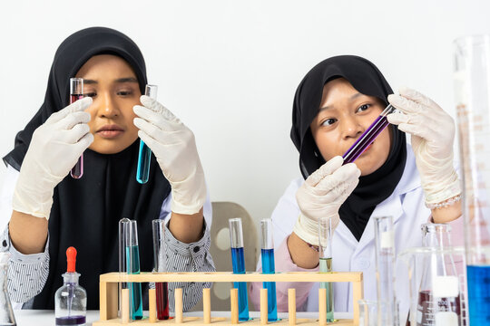 Two Muslim female scientists wearing hijab working in a chemistry laboratory with glassware and chemical solutions. Perfect for STEM education, research, science, healthcare, and biotechnology concept