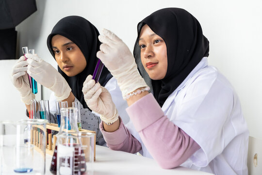 Two Muslim female scientists wearing hijab working in a chemistry laboratory with glassware and chemical solutions. Perfect for STEM education, research, science, healthcare, and biotechnology concept