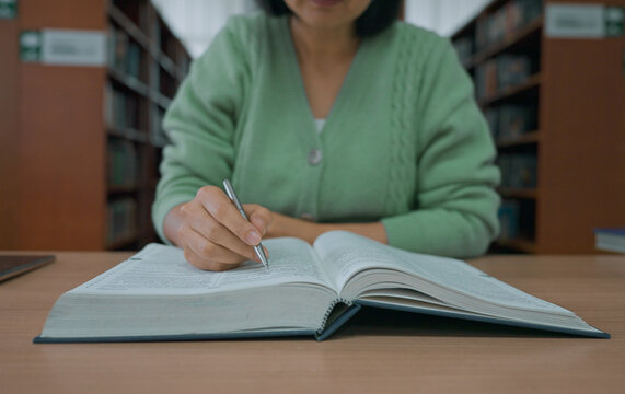 Asian woman reading book at library.
