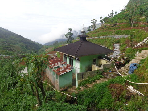 Small rural mosque located on a steep green terraced hill in mountain countryside