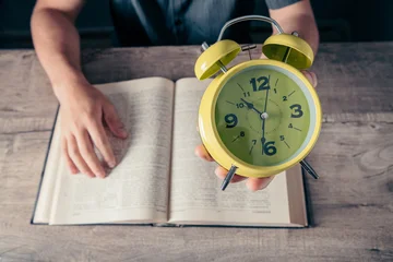Man holding alarm clock and reading a book. Time management concept. © Artvibe