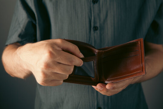 A man in a blue shirt holds an empty wallet in his hands