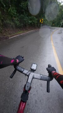 Vertical POV footage of a cyclist riding through a wet mountain curve after rain, featuring reflective asphalt, tropical forest, winding roads and a realistic outdoor adventure.