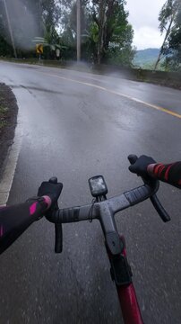 Vertical POV footage of a cyclist riding through a wet mountain hairpin curve after rain, featuring reflective asphalt, tropical forest and a scenic outdoor adventure route.
