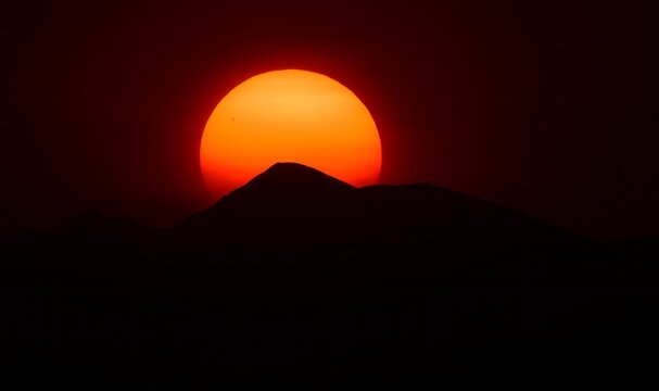 an eerie sunset of the sun sinking behind the front range of the colorado rocky mountains, through the smoke of the western forest fires , as seen from broomfield