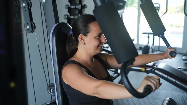 Young woman in black sportswear seated at a chest press machine in a gym performing a strength training exercise. Indoor fitness concept
