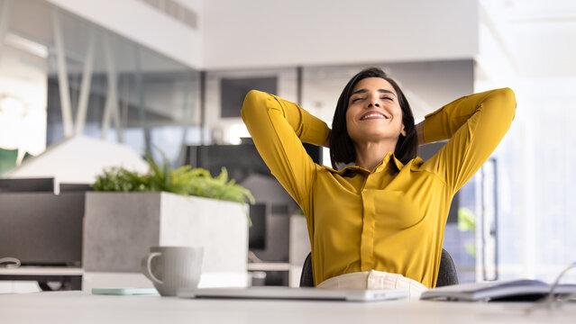 Peaceful female office employee take break lean on chair, enjoying workday end, put hands behind head, daydreaming, feeling happy and satisfied with work result, stress-free workflow and relaxation