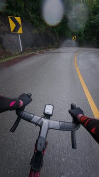 Vertical POV footage of a cyclist riding through a wet mountain bend after rain, featuring reflective asphalt, tropical forest, guardrails and a scenic outdoor adventure.