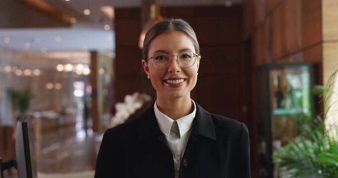 Young woman, receptionist of business or resort hotel, dressed in formal attire posing for camera in lobby or registration front desk. Guests services, head shot portrait of apart-hotel staff member