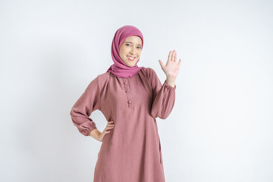 Friendly young Asian Muslim woman in hijab waving hand saying hello on white background