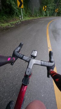 Vertical POV footage of a cyclist riding on a wet winding mountain road after rain, featuring reflective asphalt, tropical forest, gentle curves and an immersive adventure.