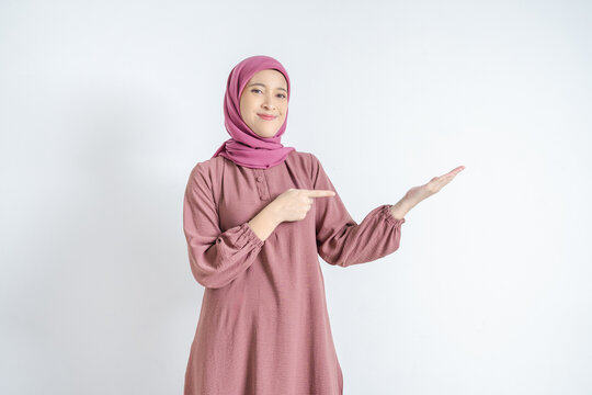 Smiling Asian Muslim woman in hijab pointing finger to open palm presenting product or copy space