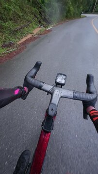 Vertical POV footage of a cyclist riding on a smooth wet mountain road after rain, featuring reflective asphalt, gentle curves, tropical forest and an immersive outdoor adventure.
