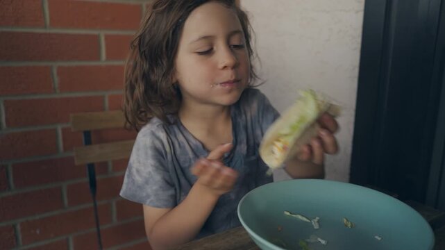 Close-up of a curly-haired child chewing a vegetable wrap