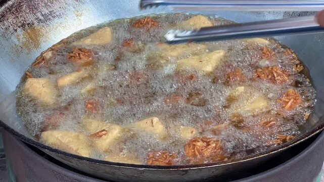 Close up shot of deep frying tofu and taro in hot boiling oil in big wok street food.