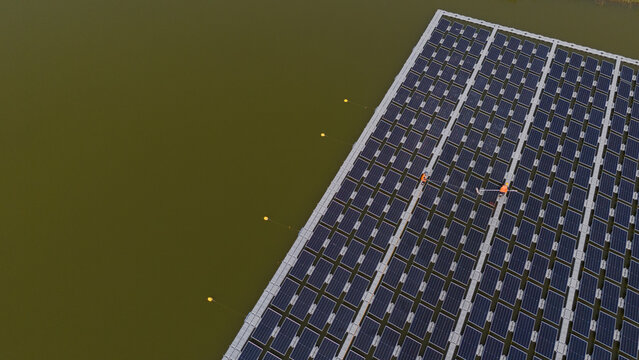 An aerial view shows workers cleaning solar panels in a large body of water.