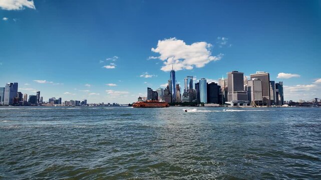 Smooth panoramic view of Lower Manhattan across New York Harbor featuring One World Trade Center, the Financial District and the iconic orange Staten Island Ferry on a sunny summer day.