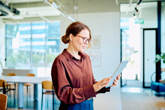 Professional businesswoman smiling, using a digital tablet in a bright, contemporary office space, symbolizing productivity and technology