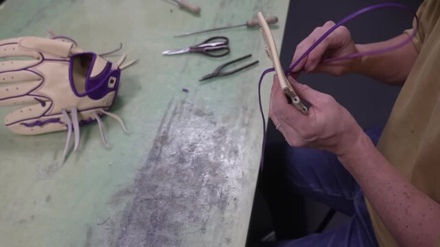Worker threading purple lace through a baseball glove with a lacing needle at the bench