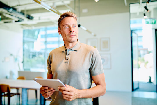 Confident man holding a tablet, looking away with vision and ambition in a contemporary office setting