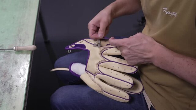 Seated craftsman hand lacing a leather baseball glove with purple rawhide lace