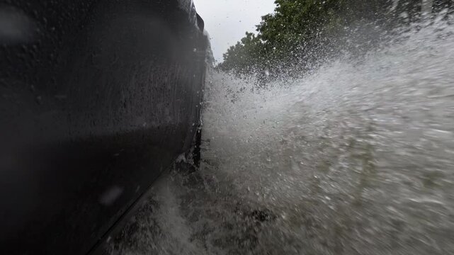 Moving car tire splashing through deep standing water during heavy rain. Dramatic view of hydroplaning risk, road flooding, and dangerous driving conditions in a severe rainstorm. Extreme Slow motion