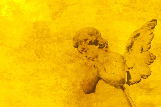 Angel cherub figure praying on a grunge gold background backdrop. Religious christian concept.