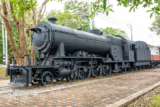 Vintage black steam locomotive train engine parked on display outdoors surrounded by green trees