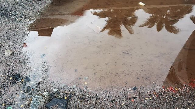 Reflections of movement of people and vehicles in rainwater collected in a roadside pothole, creating an abstract urban landscape after rainfal