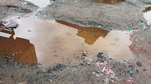 Reflections of movement of people and vehicles in rainwater collected in a roadside pothole, creating an abstract urban landscape after rainfal